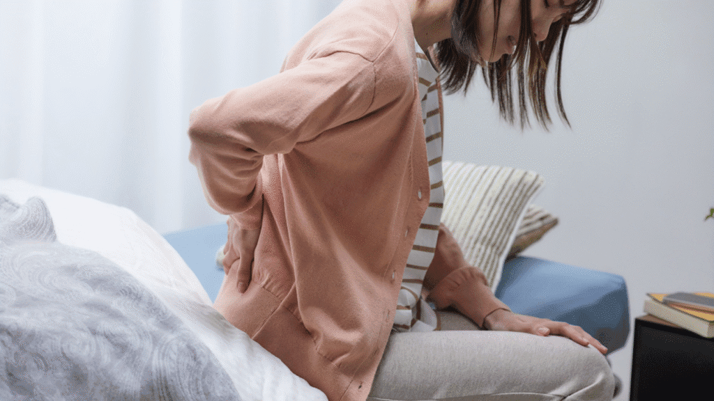 Woman sitting and holding her lower back, showing pelvic pain and need for pelvic floor therapy