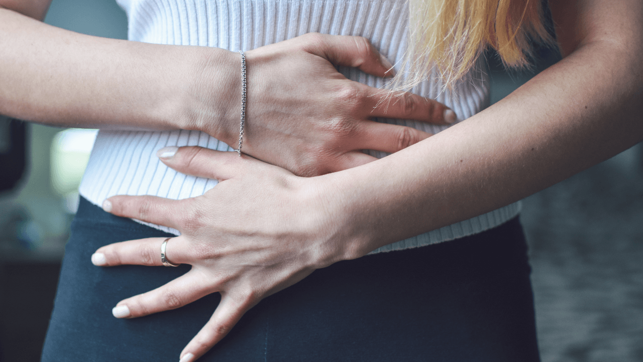 Woman holding her stomach and pelvic area due to pain and discomfort from poor pelvic health.